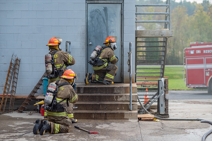 A group of firefighters stands on the steps of a building, ready for action in their uniforms and gear.