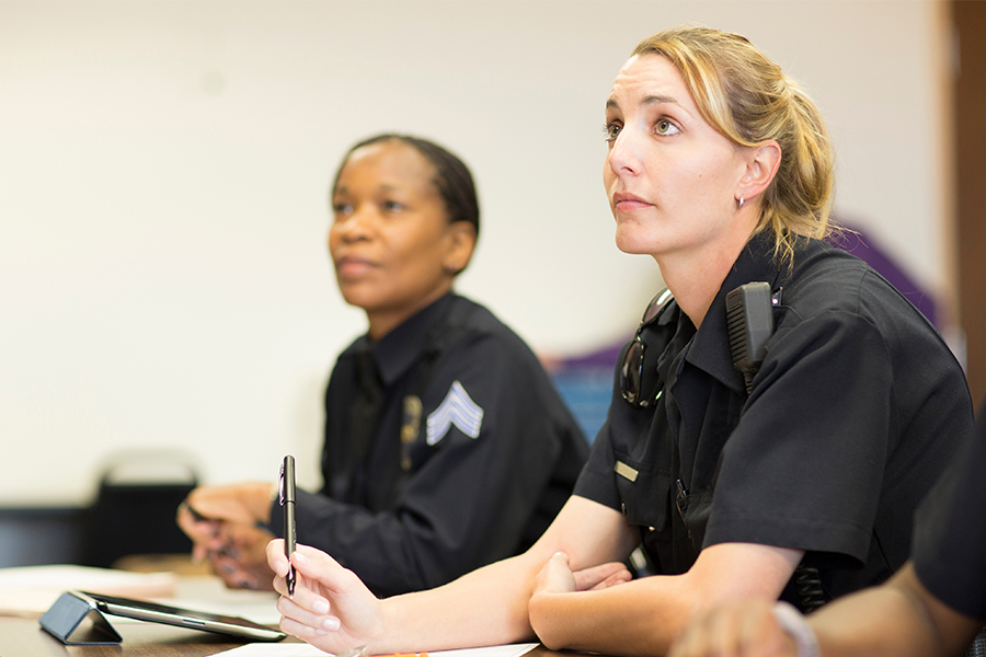 Two police officers in uniform attentively listen during a meeting. One officer takes notes, conveying focus and professionalism.