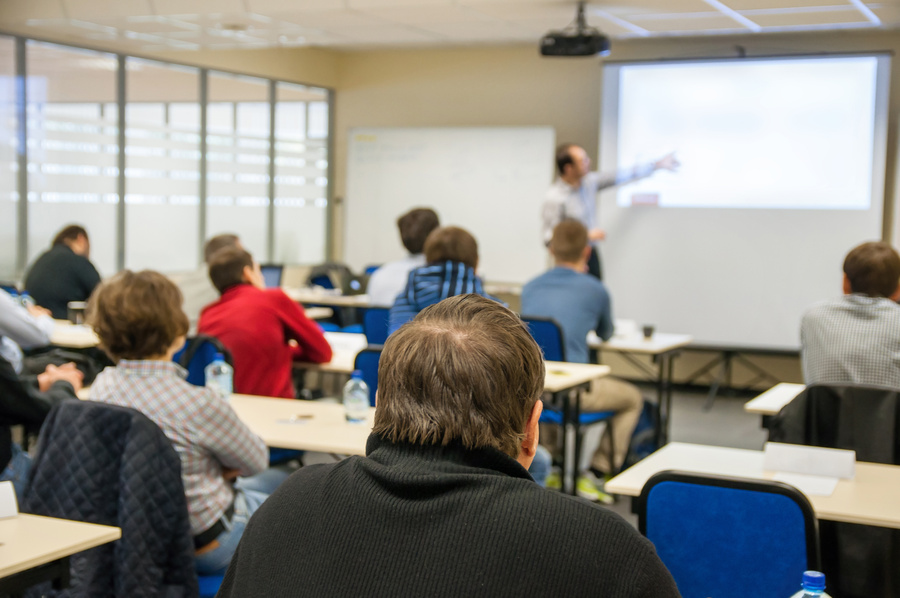 People sit in a classroom-style training session facing a presenter who is pointing to a projected presentation at the front of the room.
