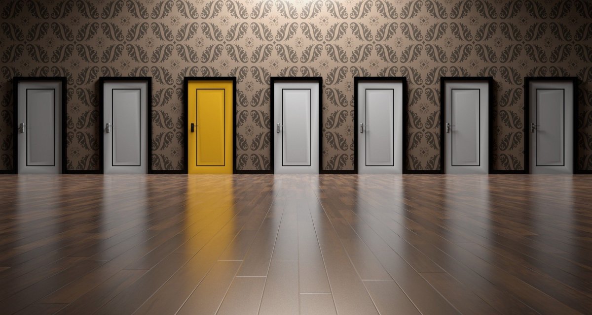 A single bright yellow door stands out among a row of six identical closed white doors along a wall with patterned wallpaper and polished wooden flooring.